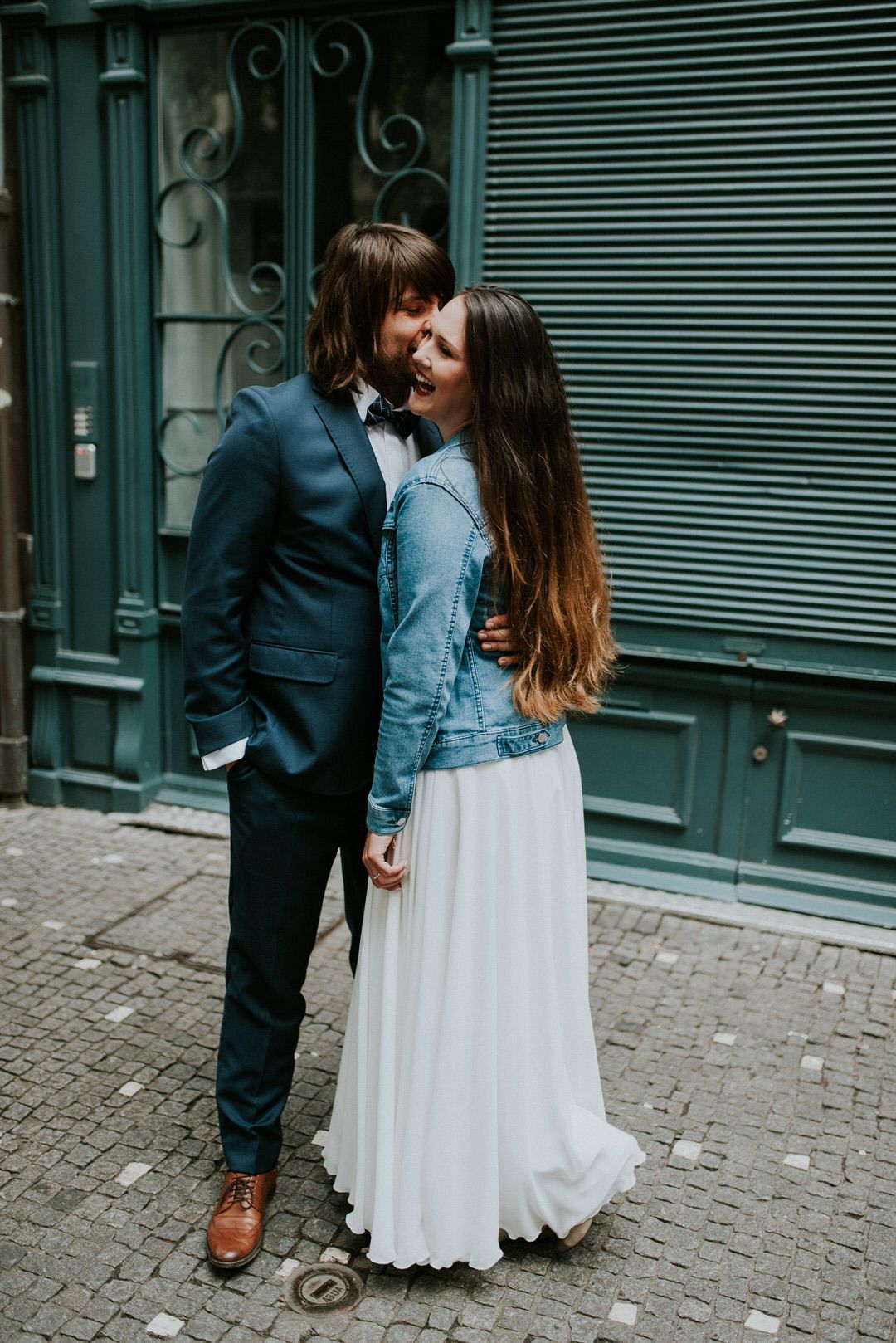 Romantic couple in formal attire sharing intimate moment against urban storefront.
