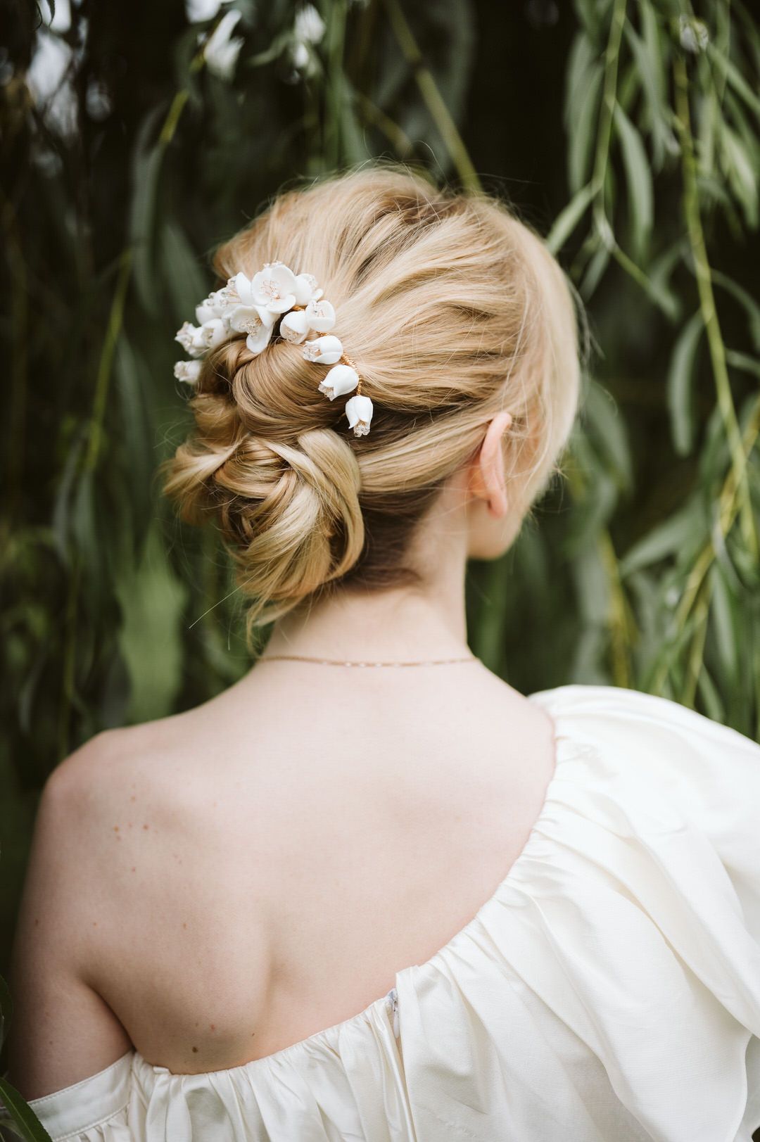 Bridal updo hairstyle with delicate white floral hair accessories against green foliage.