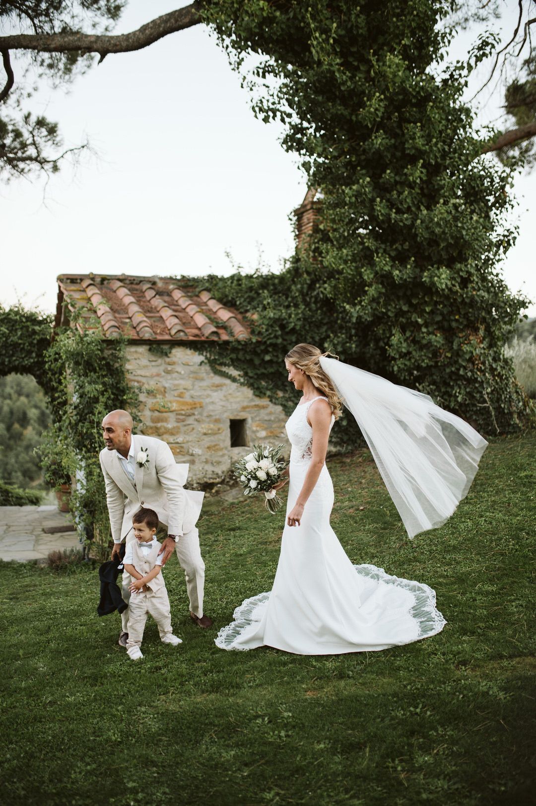 Wedding scene in garden with flowing veil and stone cottage in background.