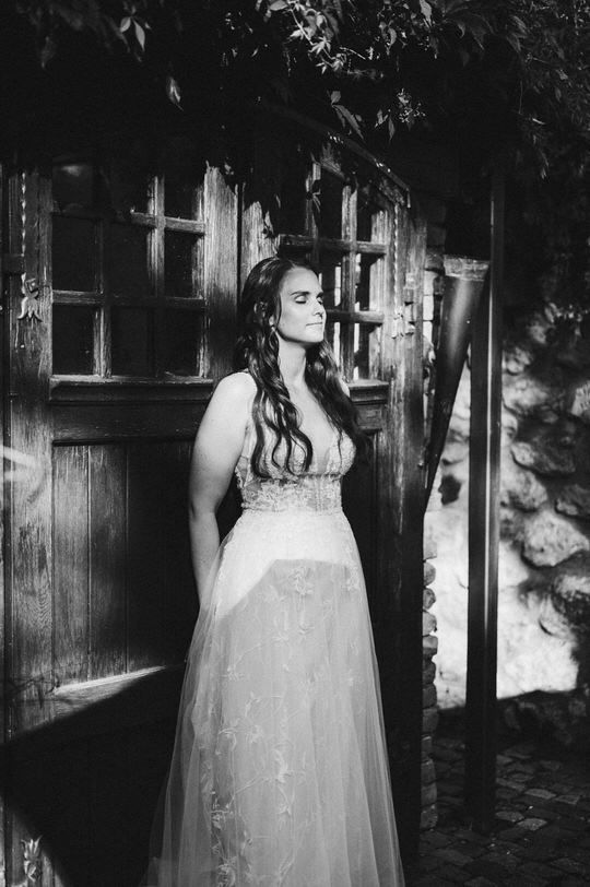 Dramatic black and white portrait of bride in lace gown against rustic wooden door.