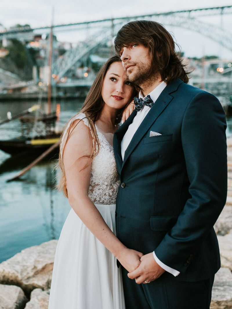 Romantic wedding portrait by harbor with bridge and boats in background at dusk.