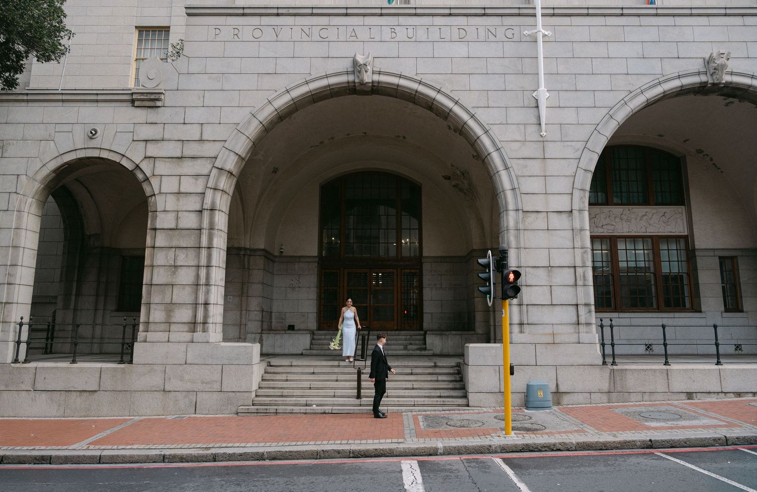 A long panoramic view of a stone building exterior with arched windows and walkways along a street.