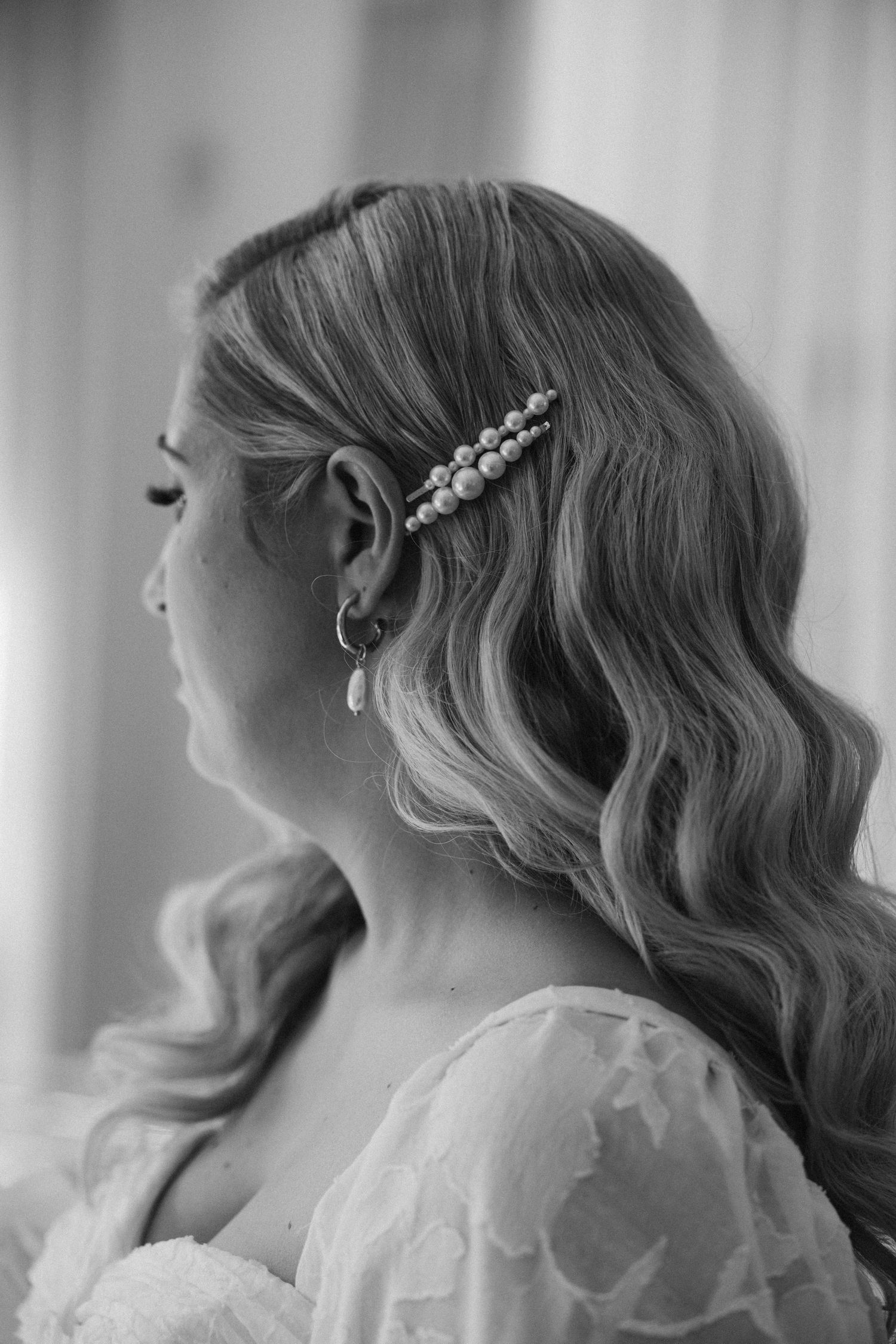 A close-up side view shows wavy blonde hair styled with a pearl hairpin for a wedding look in black and white.