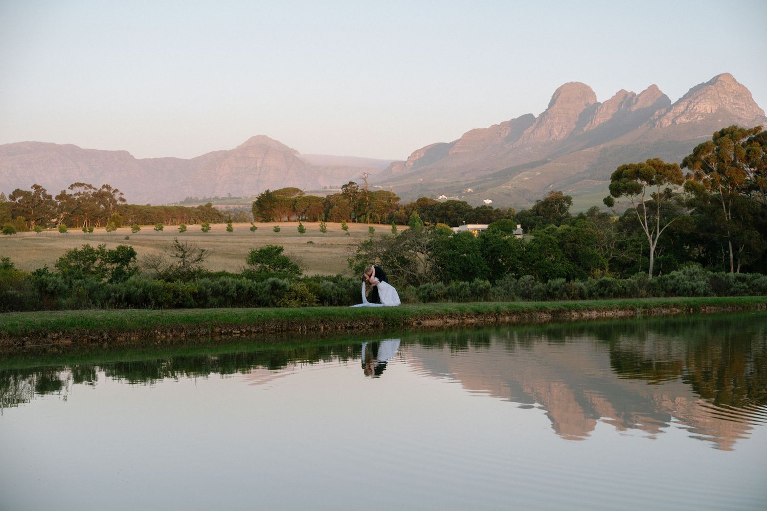 Scenic mountain landscape with lake reflection and wedding couple silhouetted in distance.