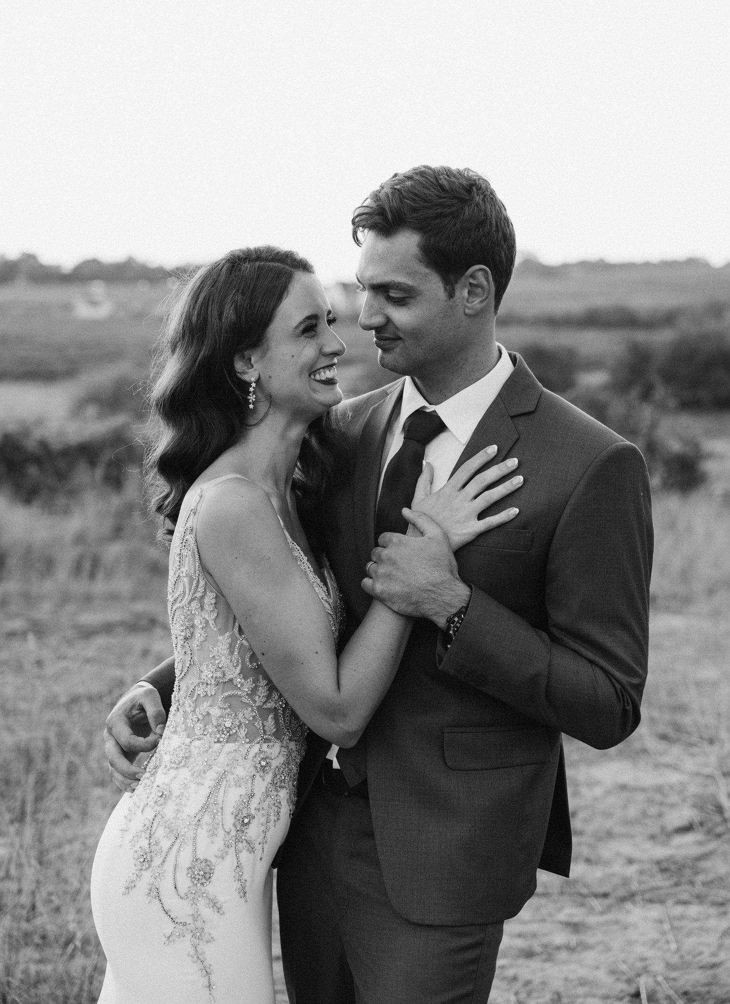 A romantic black and white wedding photo of a couple embracing outdoors with a scenic landscape in the background.
