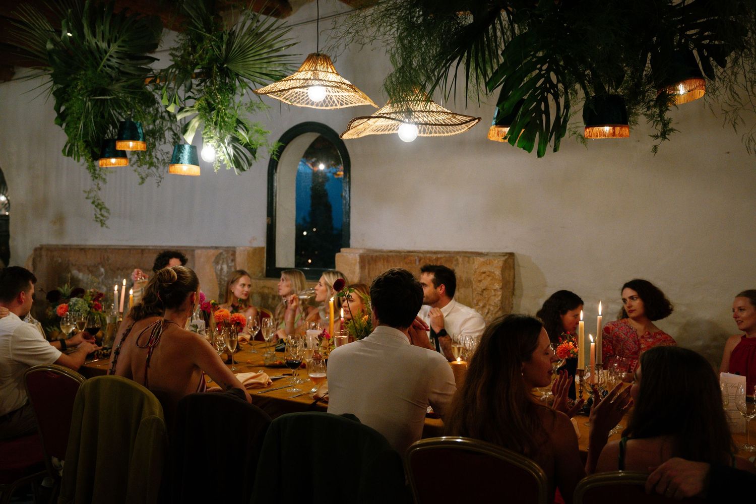 Dimly lit restaurant interior with guests dining at tables under hanging plants and pendant lights.