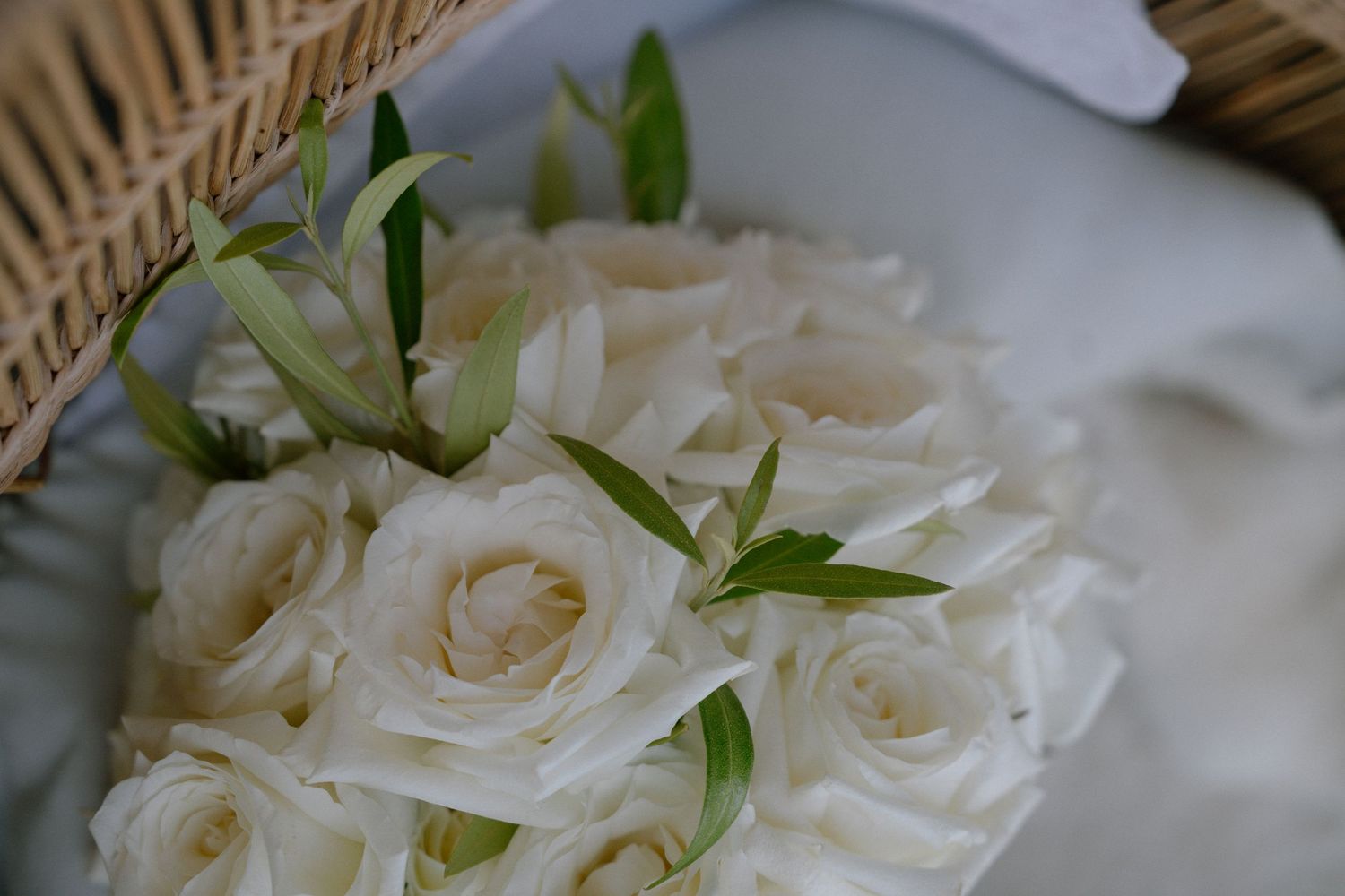 Detailed view of fresh white roses arranged with green leaves in soft lighting for wedding.