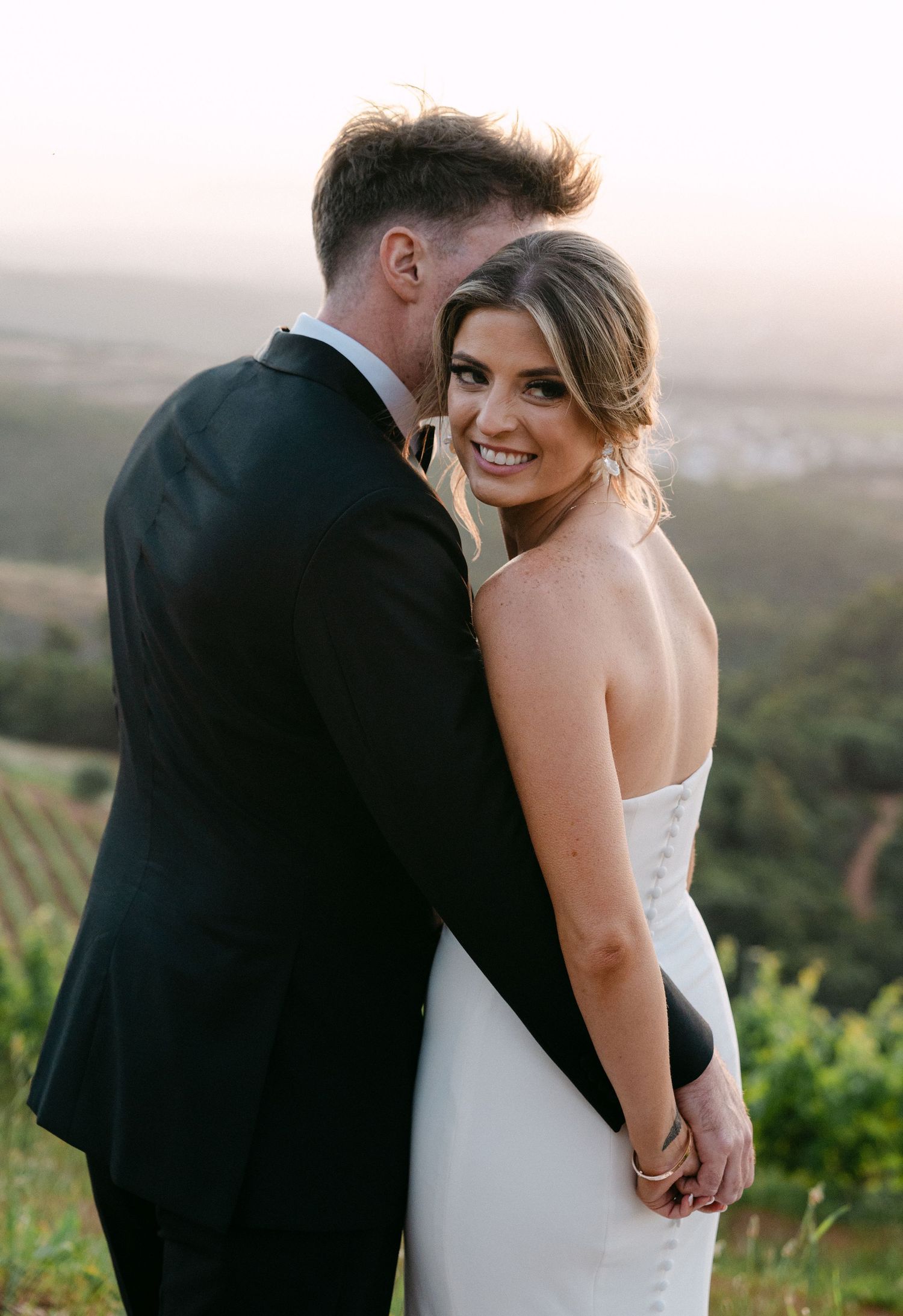 A romantic wedding moment captured on a hilltop overlooking a scenic valley at sunset.
