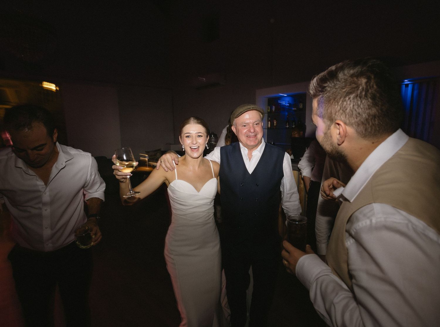 Wedding guests dancing and celebrating together on a dimly lit dance floor during an evening reception.