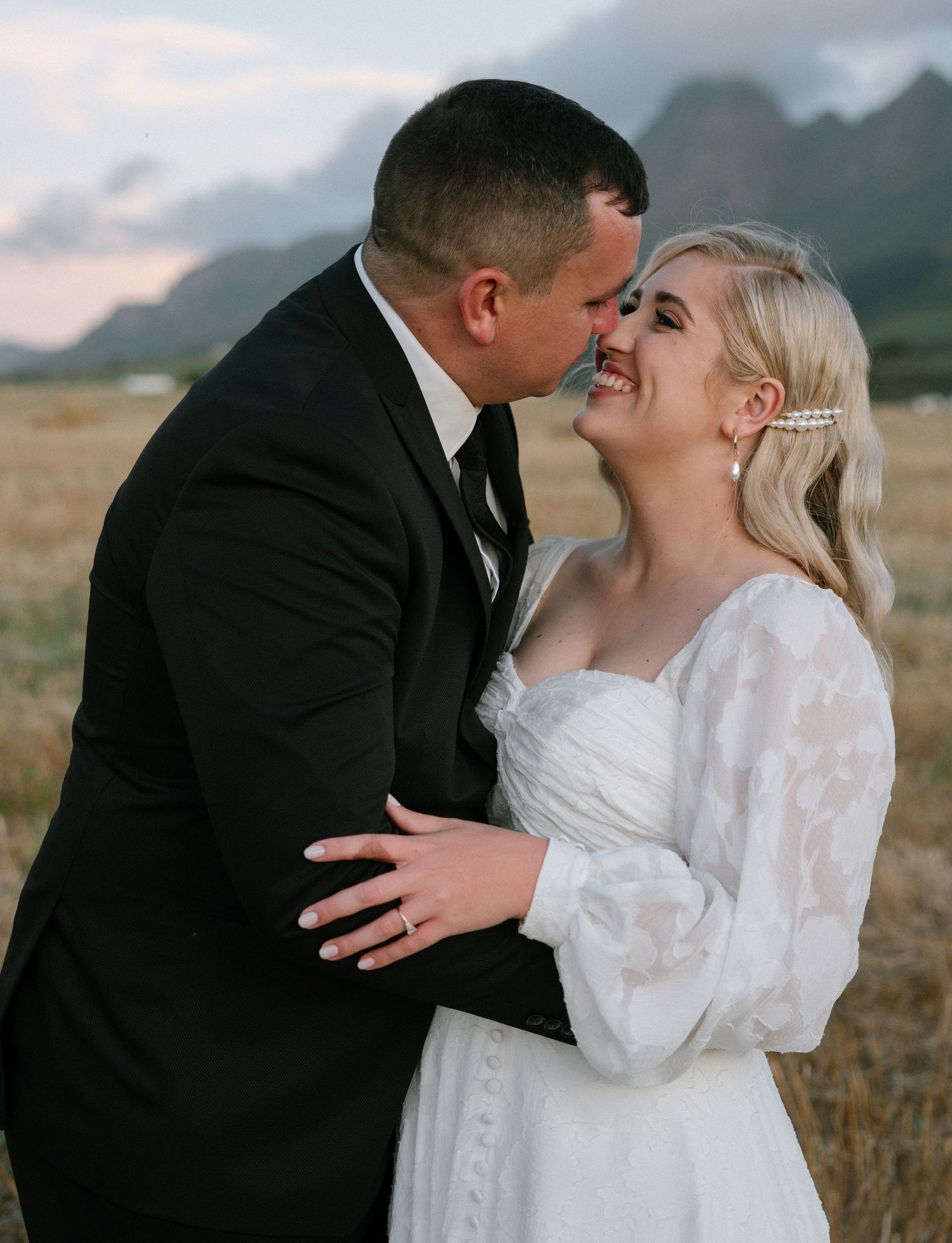 An intimate wedding portrait showing a tender moment against mountain scenery.