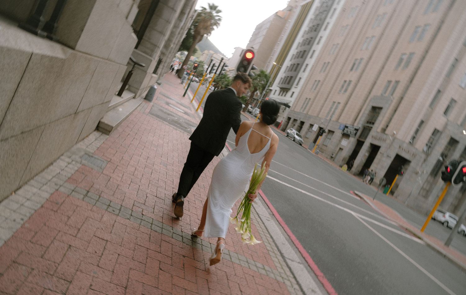 People walking along a sidewalk in an urban area with tall buildings on a cloudy day.