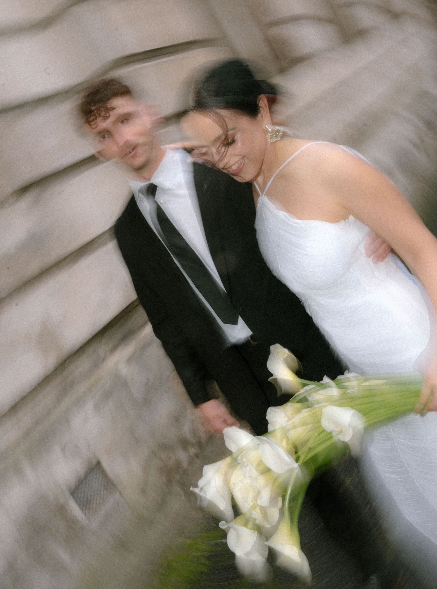 Artistic motion blur wedding photo shows couple in black suit and white dress holding calla lily bouquet.