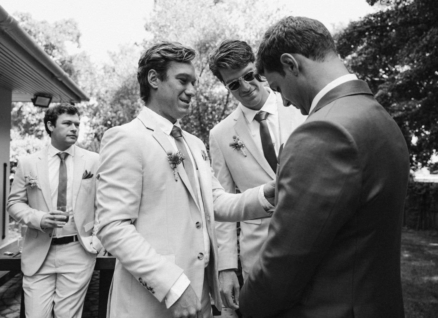 A black and white photo shows a conversation between three men in light colored suits at an outdoor gathering.