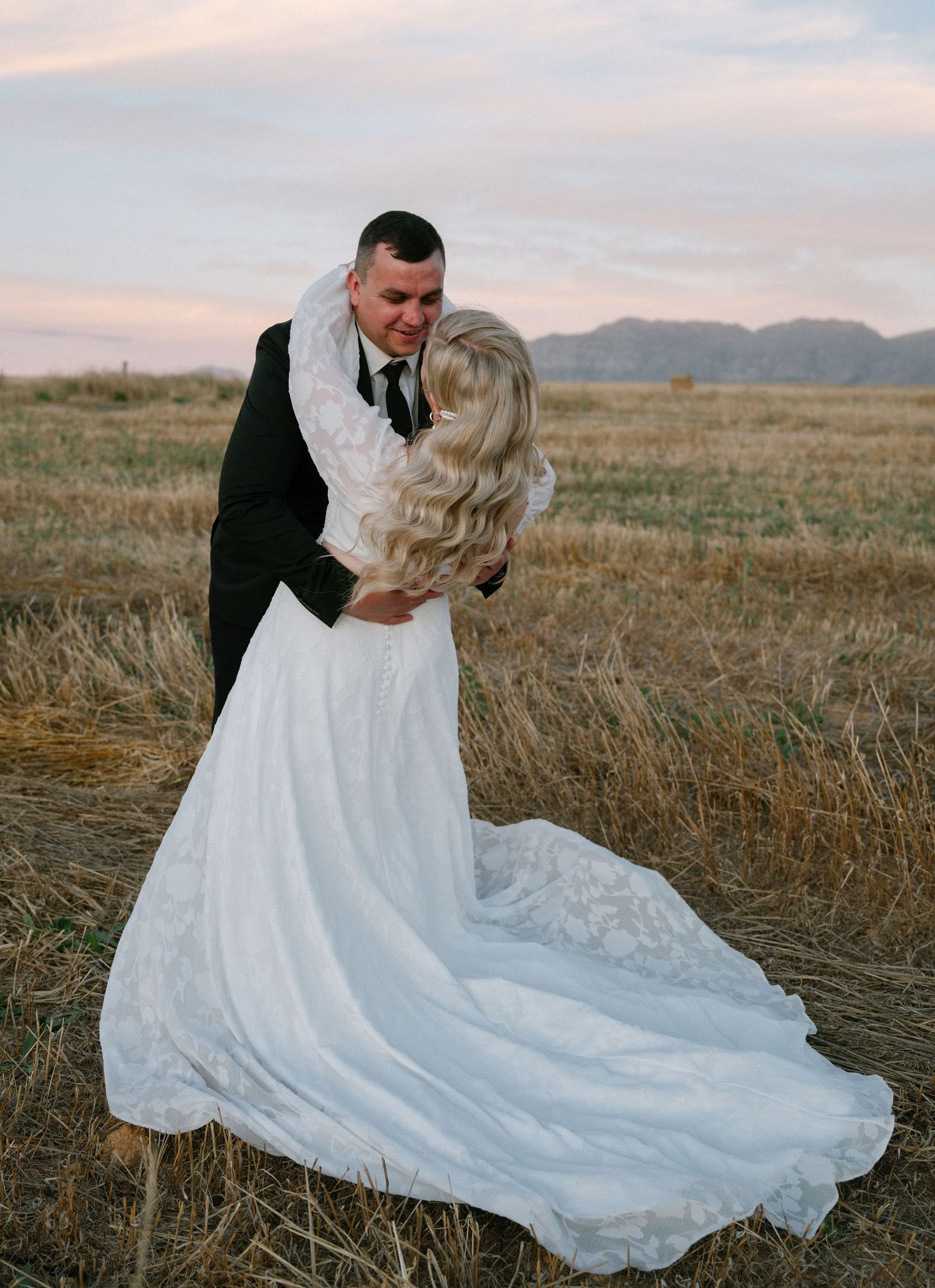 A romantic sunset wedding portrait in a field with mountains in the background.