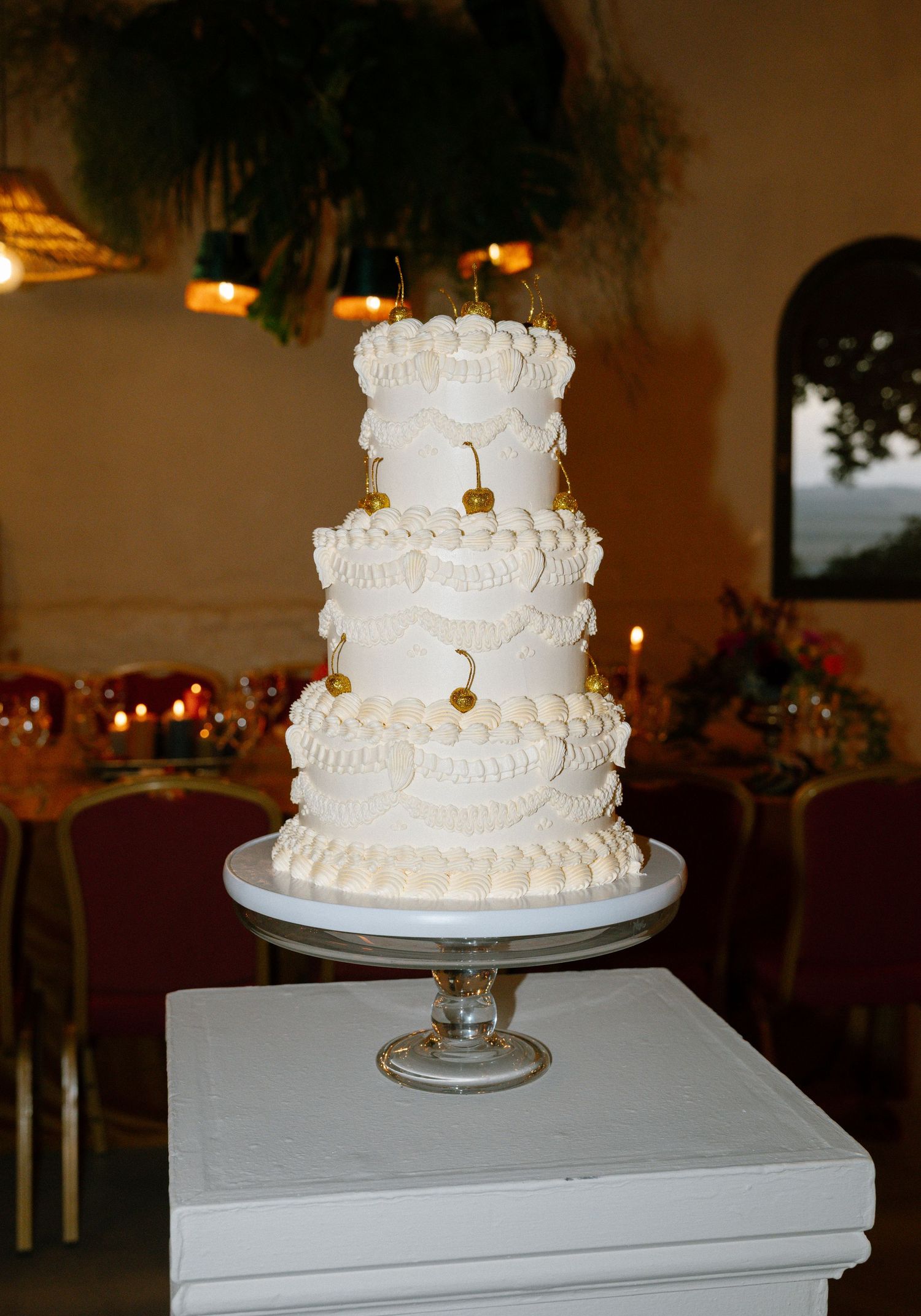 Elegant three-tiered white wedding cake with delicate piped details on a glass pedestal.