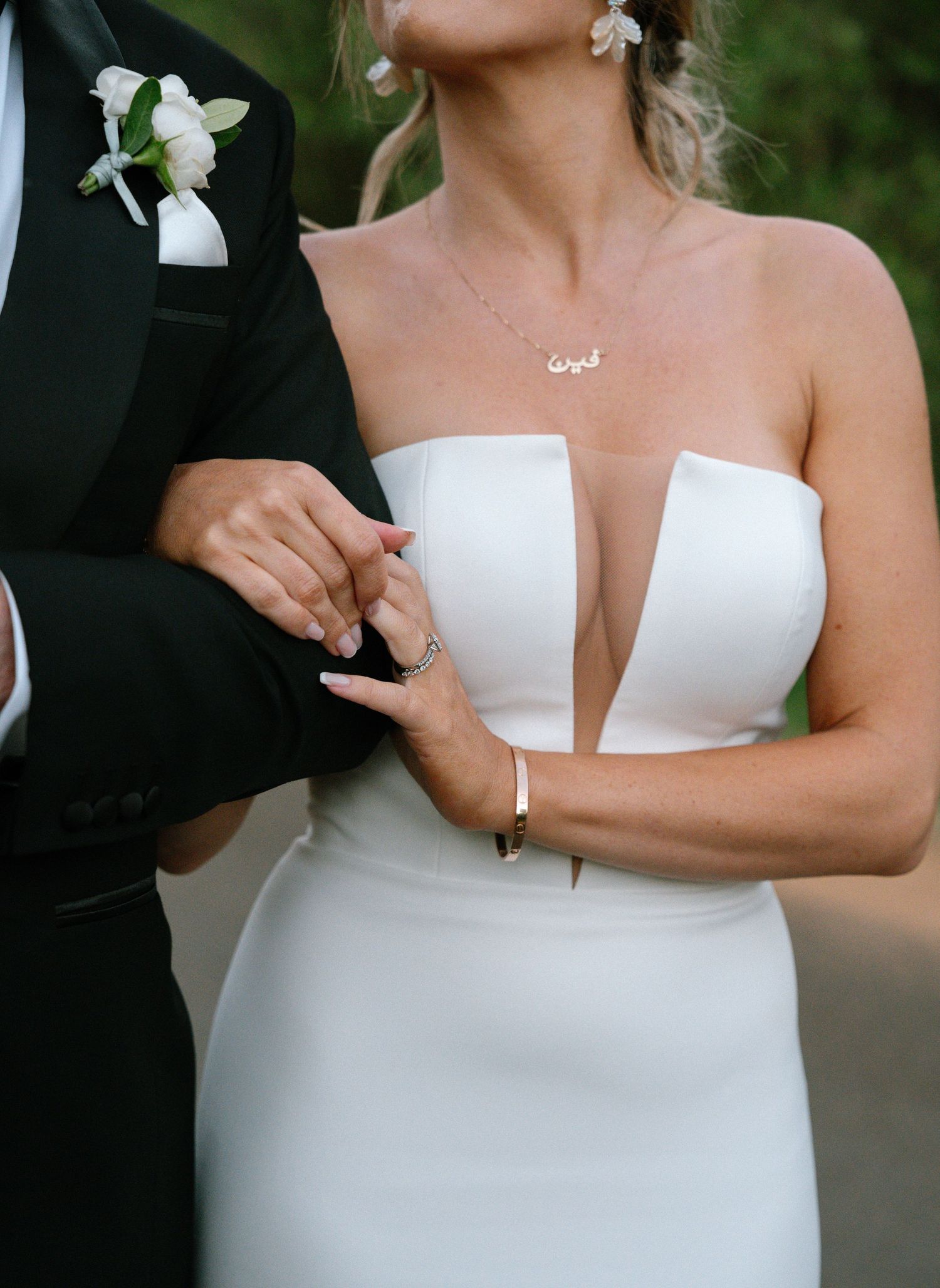 Close-up wedding photo showing the torso of a bride in white dress with plunging neckline and groom in black suit with boutonniere.