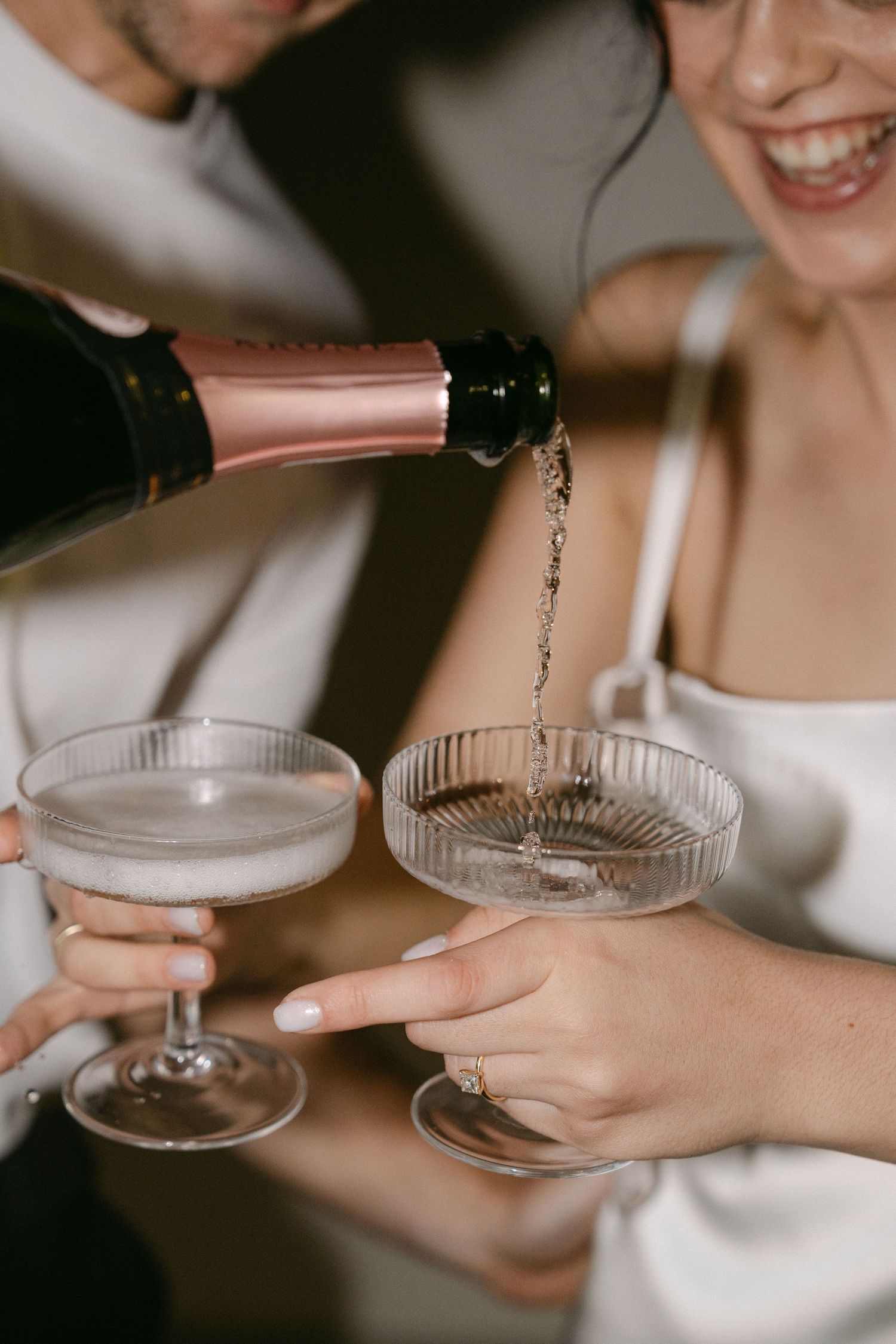 Champagne being poured into vintage coupe glasses held by hands in a celebratory moment.