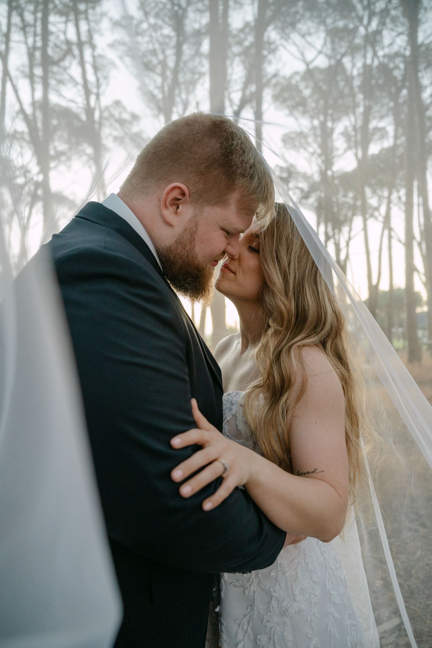 Intimate wedding portrait of couple embracing in misty forest setting.