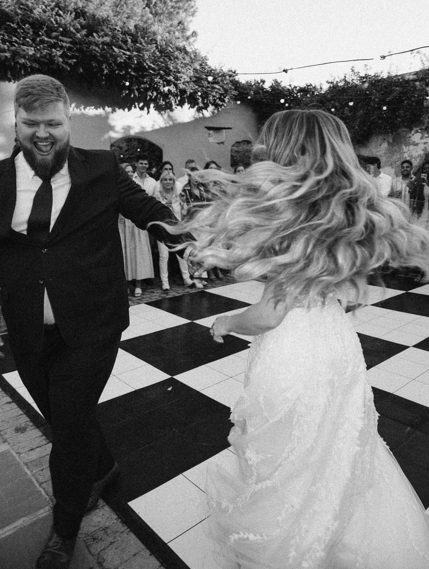 A joyful wedding dance captured in black and white on a checkered floor.