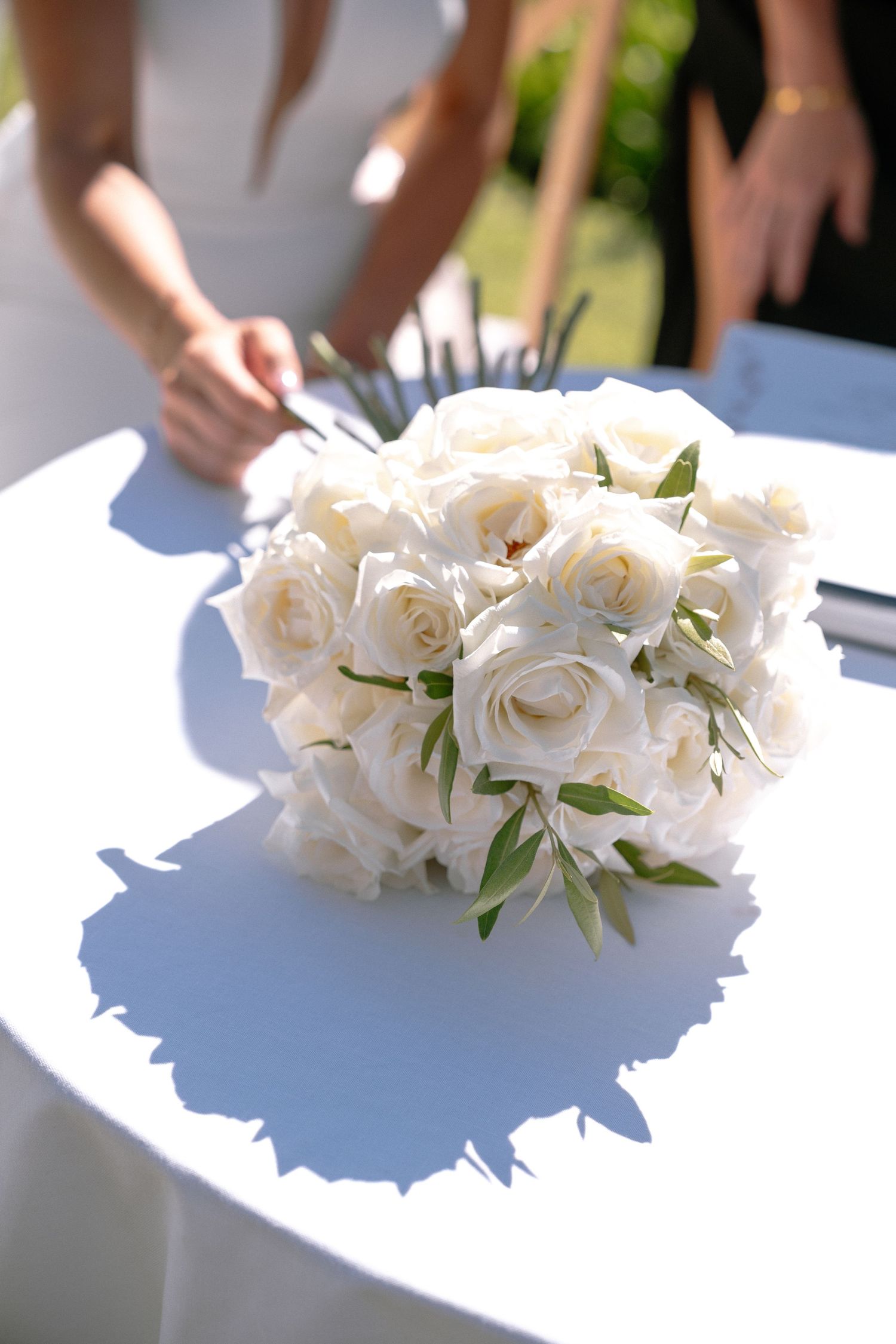 A classic white rose wedding bouquet casts a shadow on a white surface in bright sunlight.