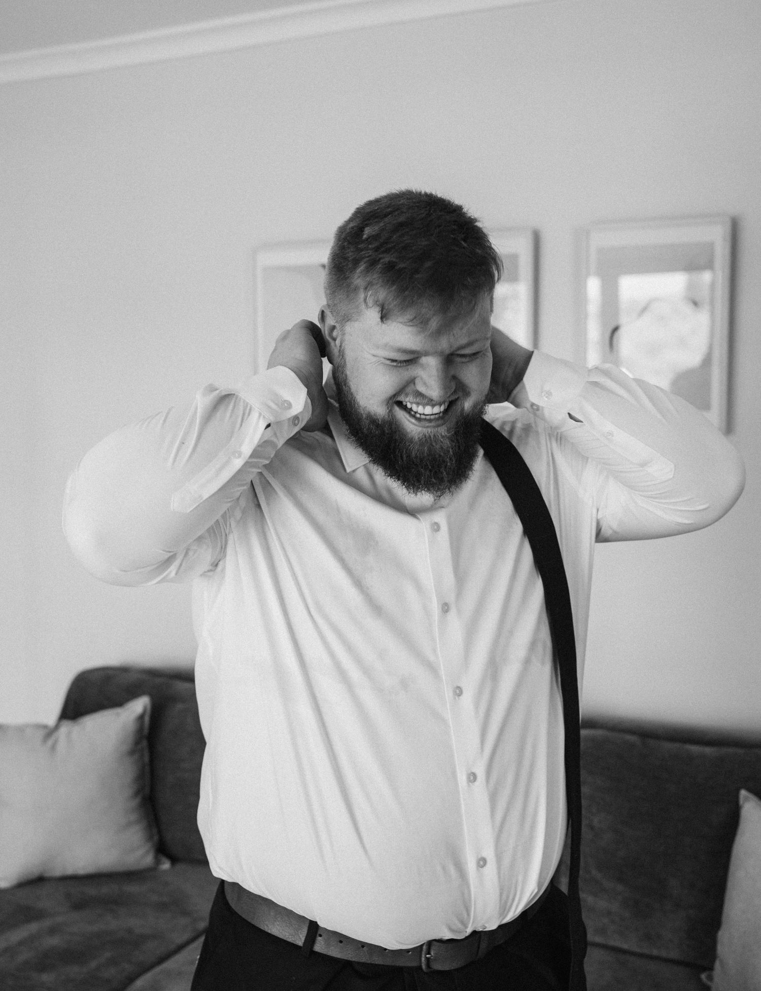 Emotional groom in white shirt and suspenders adjusting his collar while getting ready.