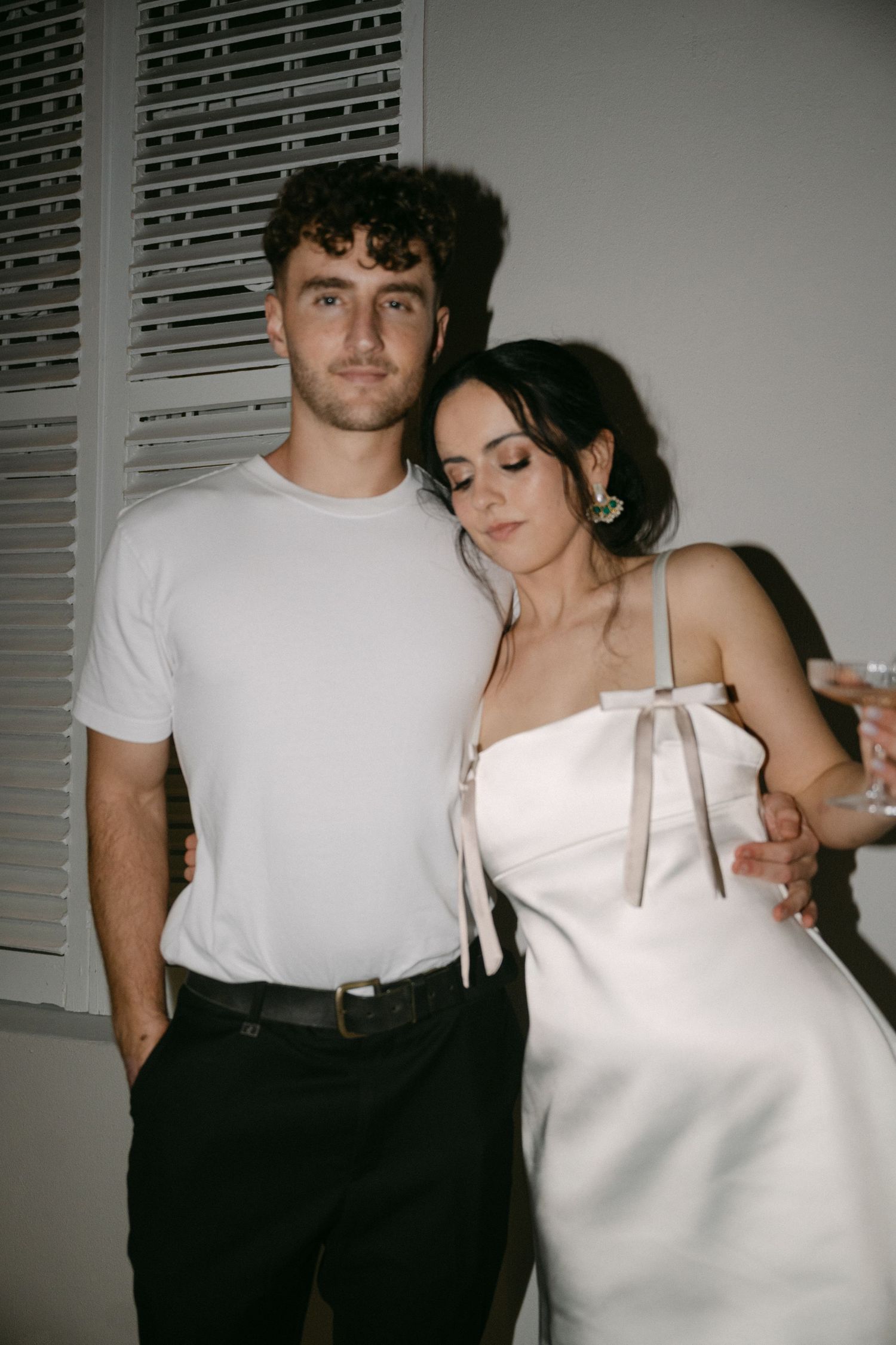 A couple in contrasting black and white outfits pose intimately together in a dimly lit room.