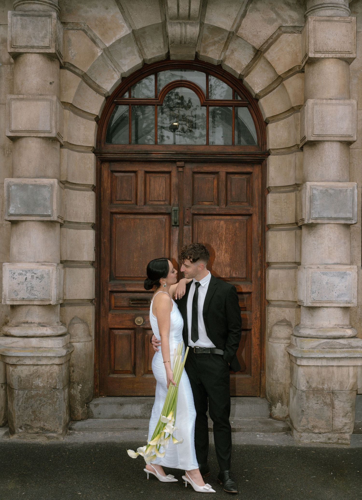A romantic wedding photoshoot in front of an ornate stone building with arched doorways.