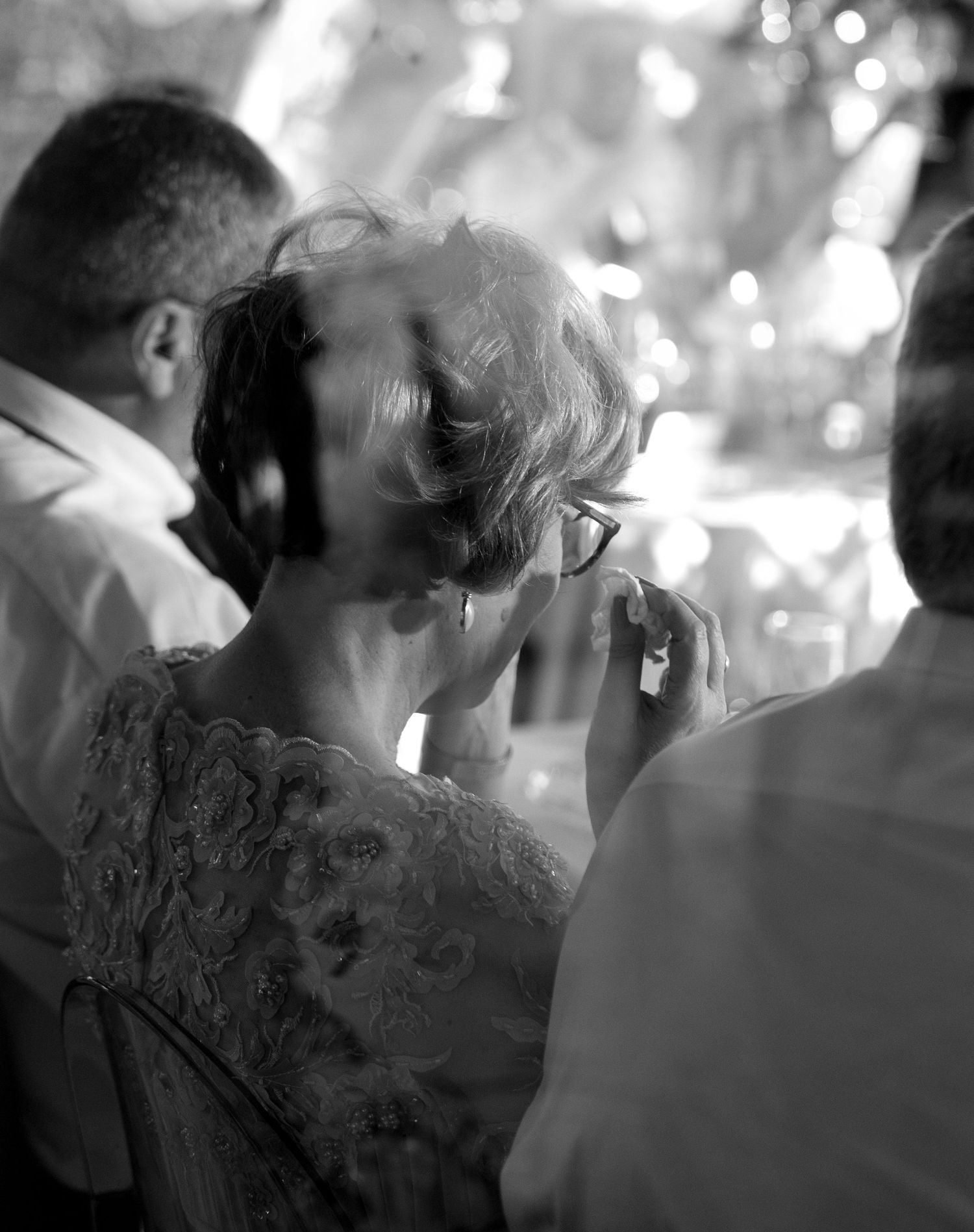 Black and white photograph of elegantly dressed people at a party with someone enjoying a drink in soft lighting and bokeh.