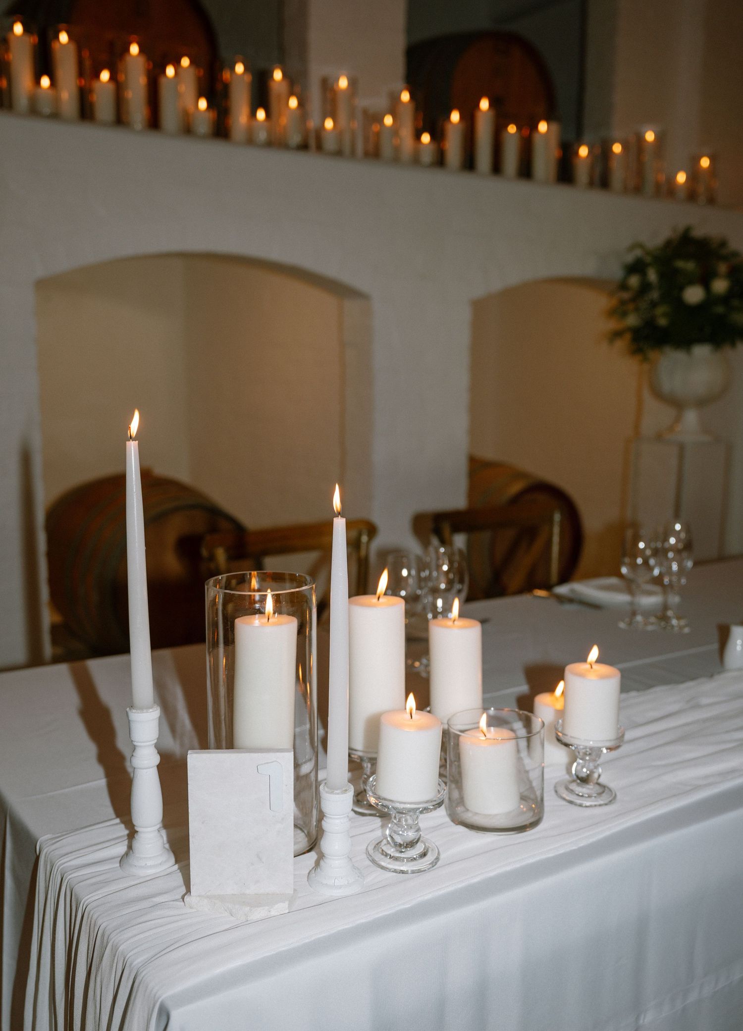 White candles of varying heights arranged on a formal table with elegant glassware.