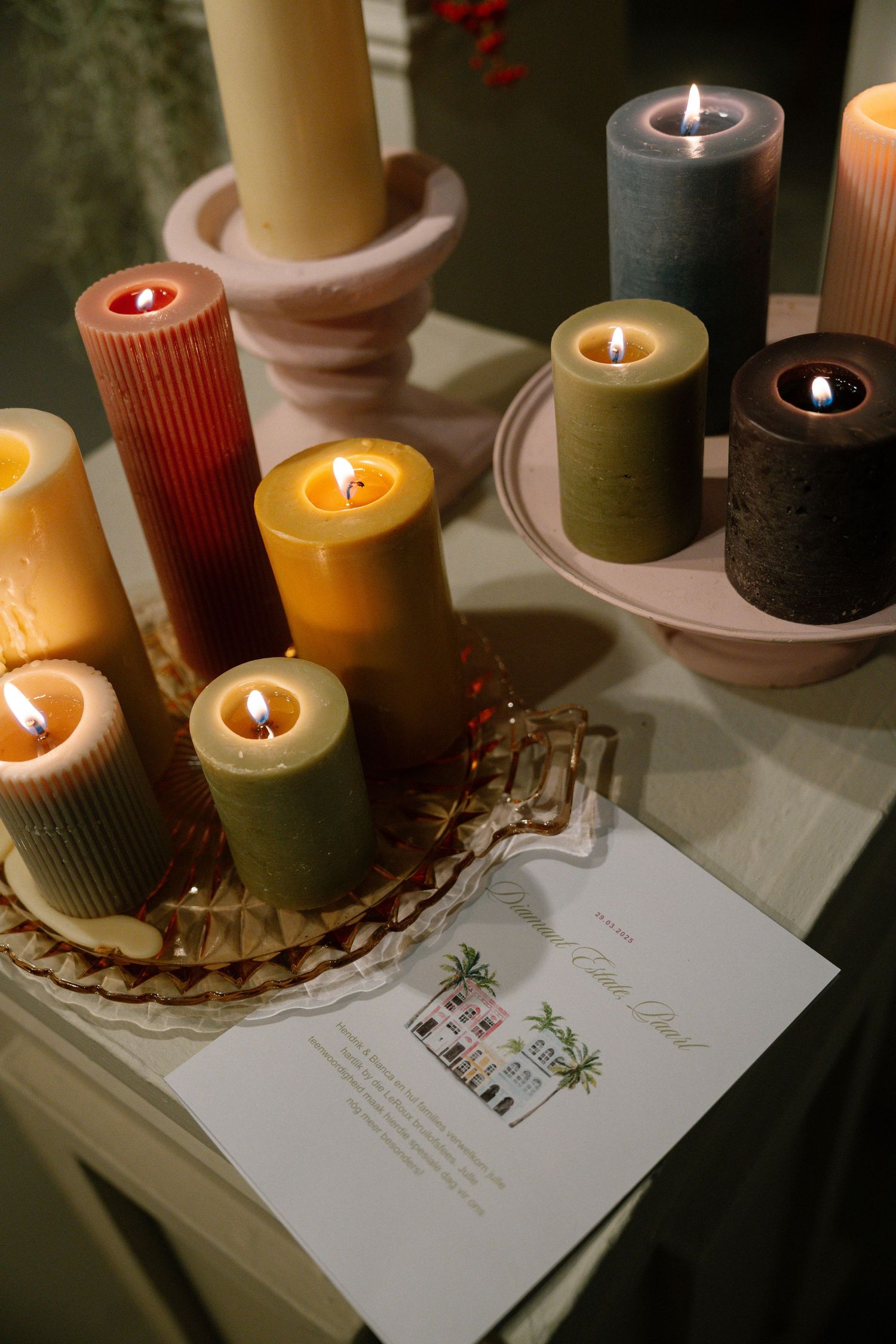Collection of colorful pillar candles arranged with a wedding invitation on a table.