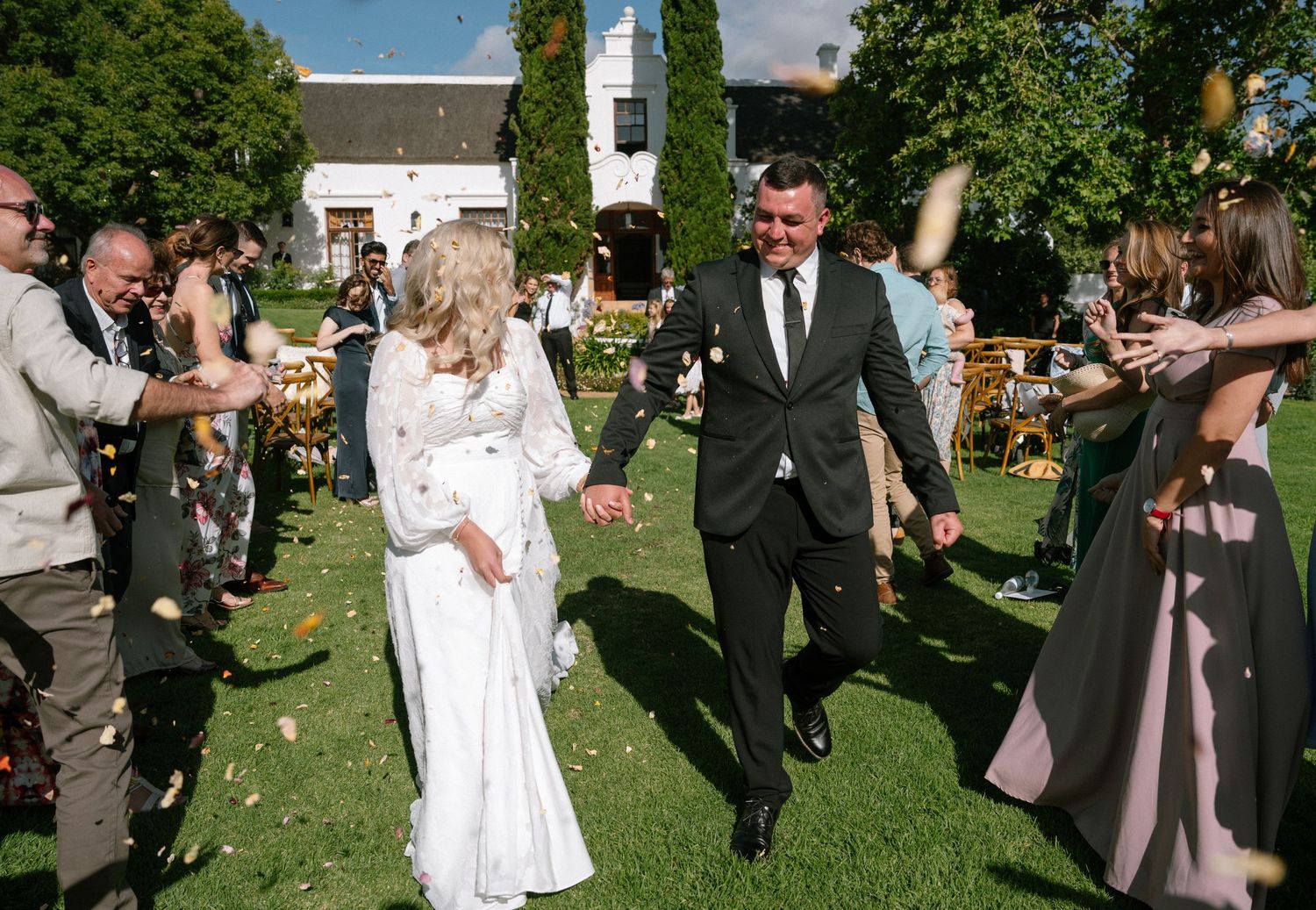 Wedding celebration in a sunny garden with guests throwing confetti.