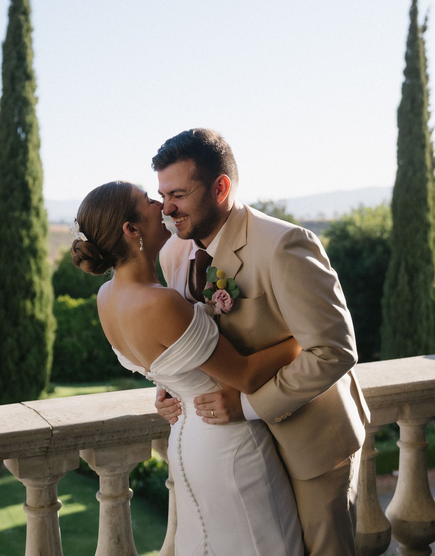 A romantic wedding moment on a balcony with cypress trees and rolling hills in the background.