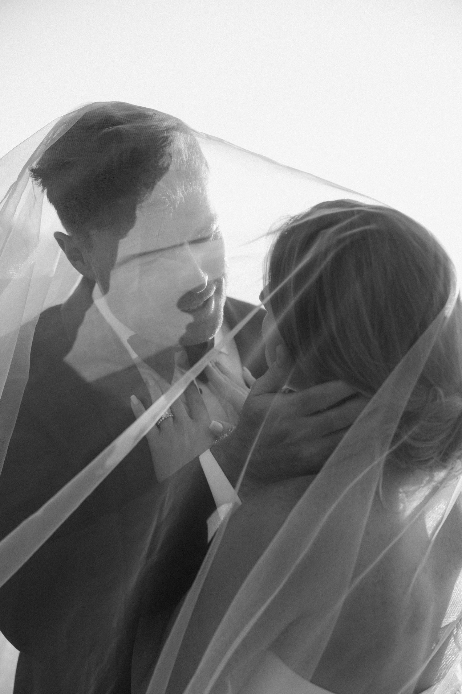 A romantic black and white wedding photo showing a tender moment between newlyweds under a sheer veil.