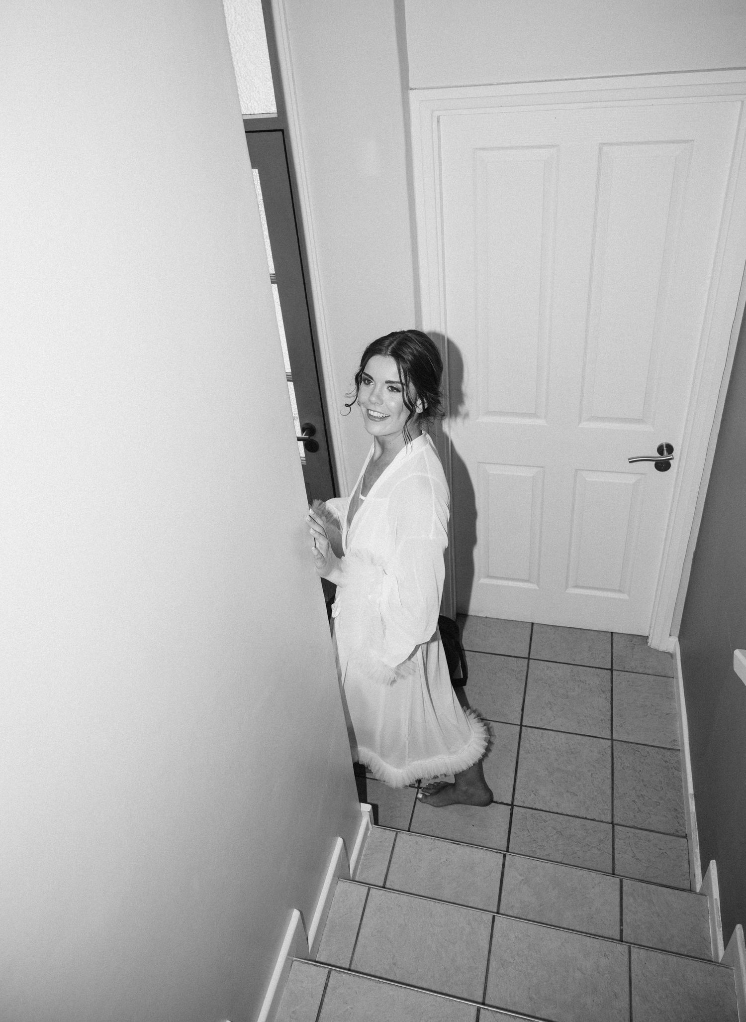 Black and white photo of a person in a robe standing on tiled stairs with a white door in the background.