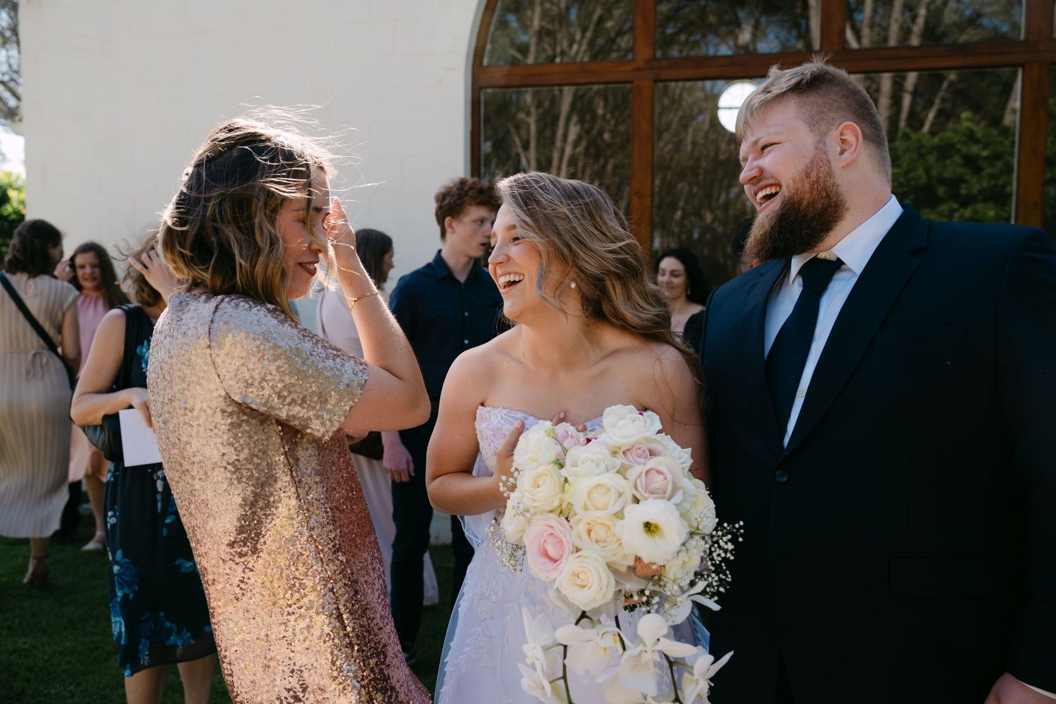Wedding party sharing joyful moment outside venue with bride holding bouquet.