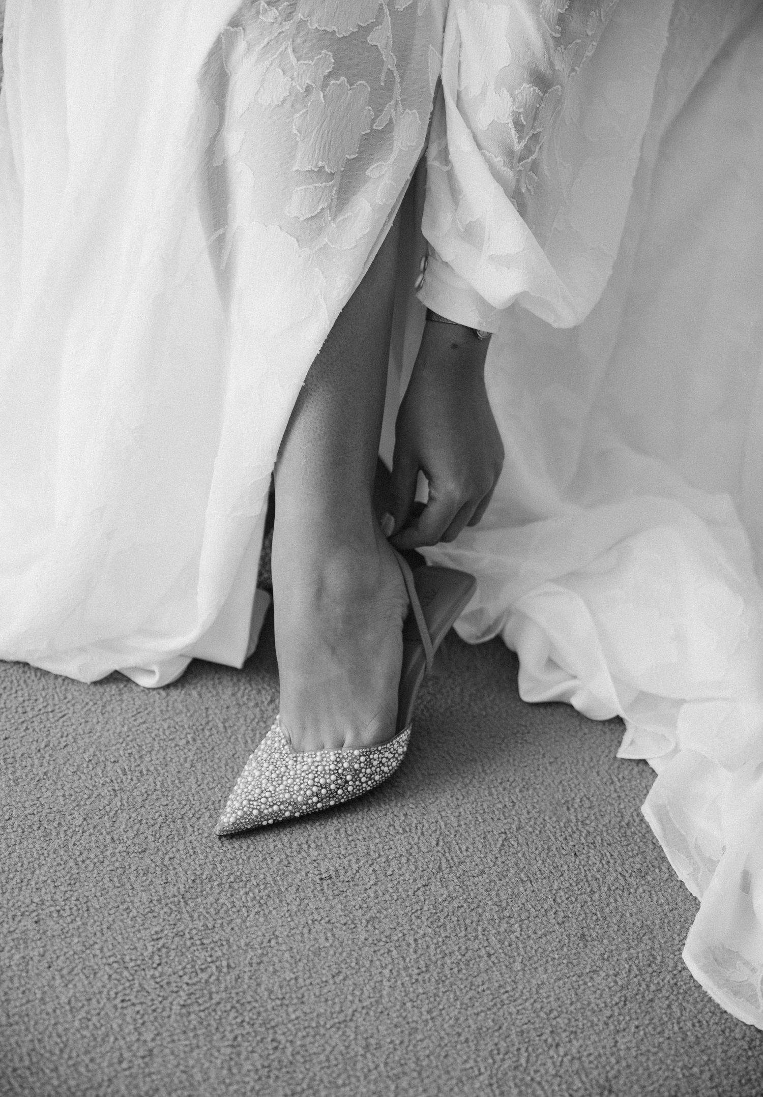 Close-up of sparkly bridal shoes peeking out from under a flowing white wedding dress.