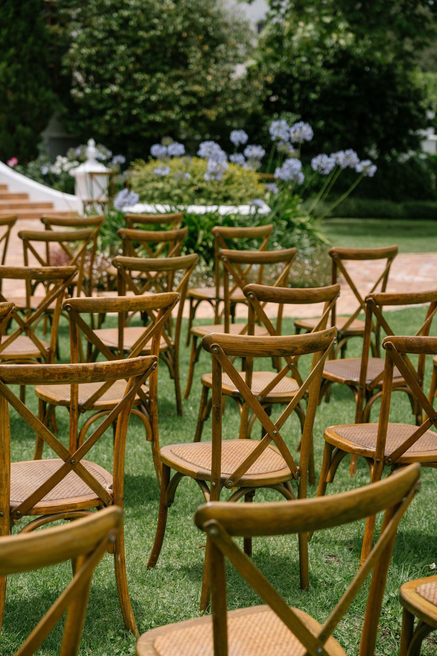 Wooden cross-back chairs arranged outdoors for a garden wedding ceremony.