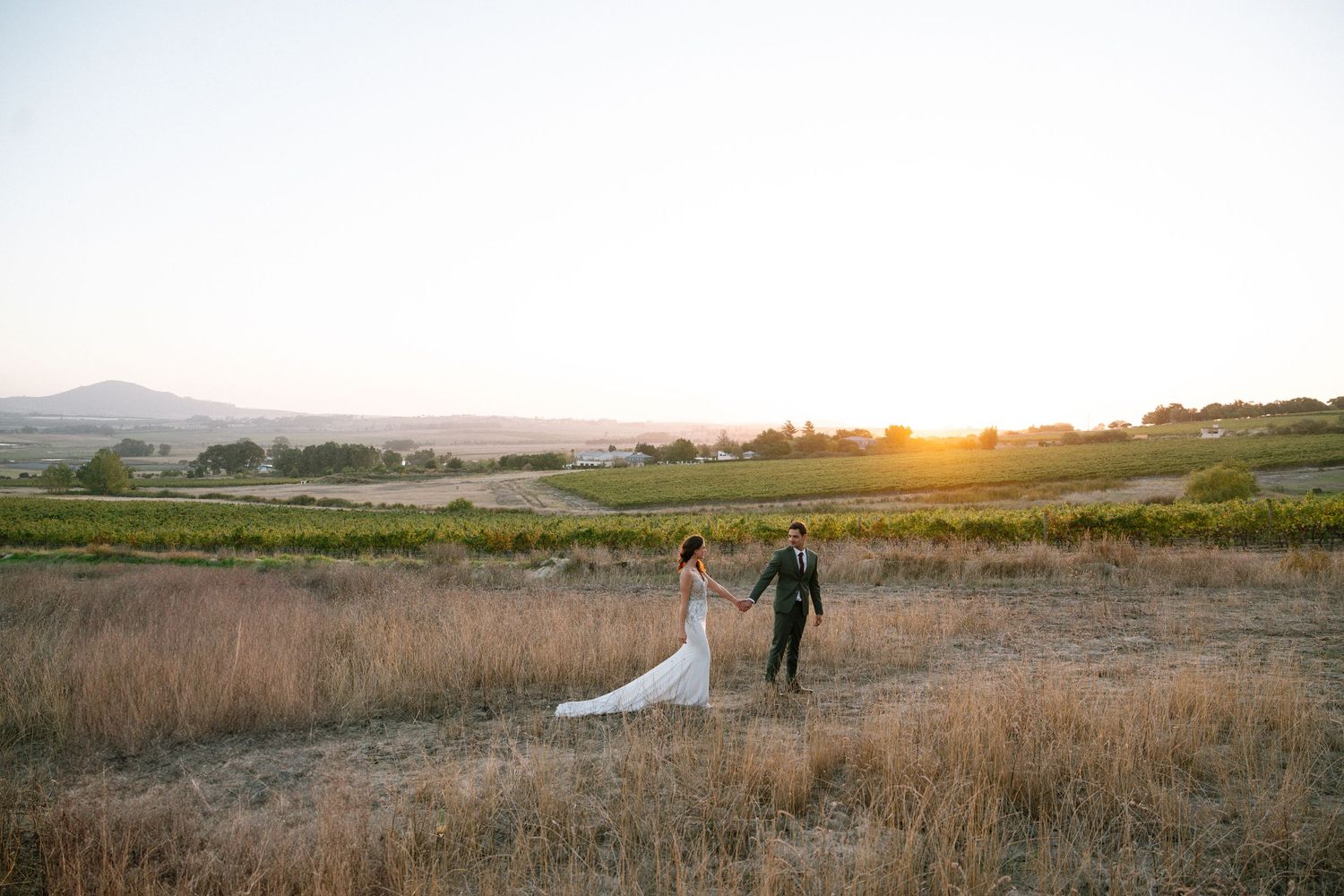 Couple walking in a golden field at sunset with rolling hills in the background.