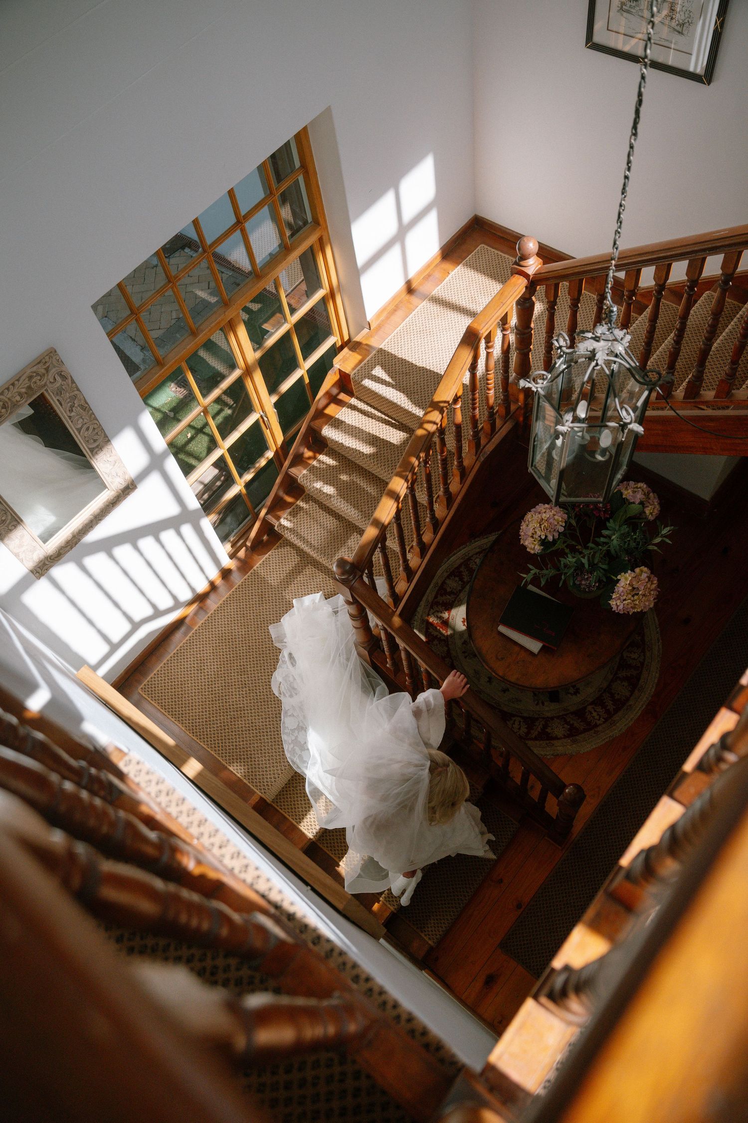 Overhead view of wooden stairs with natural light streaming through windows and white dress flowing down steps.