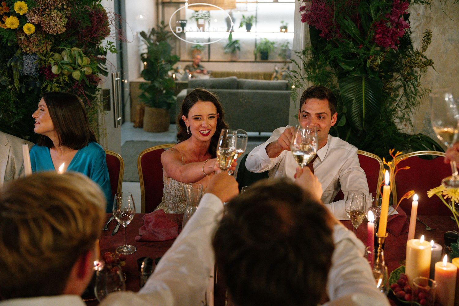 Guests raise wine glasses for a celebratory toast during an elegant candlelit dinner party at an ornate venue.