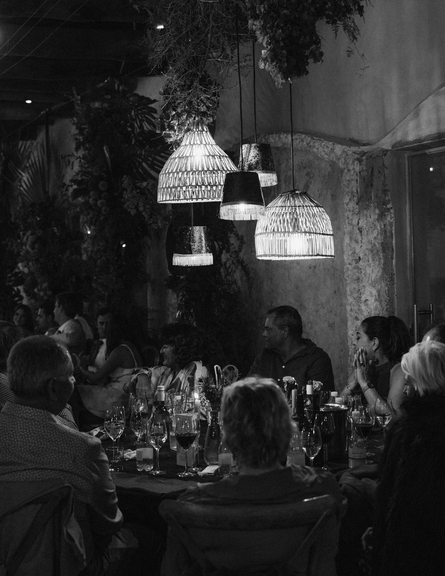Moody dinner scene with woven pendant lamps illuminating guests around a table.