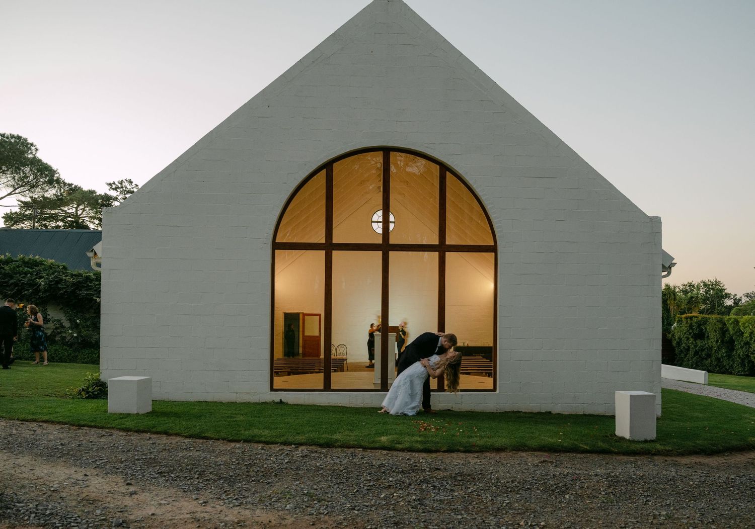 Modern white chapel with arched window glowing at dusk.