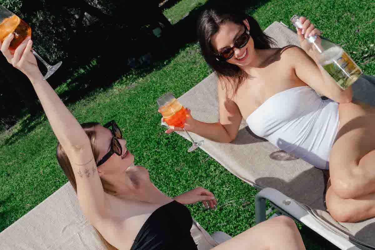Two people sunbathing on loungers while holding colorful drinks in a garden setting.