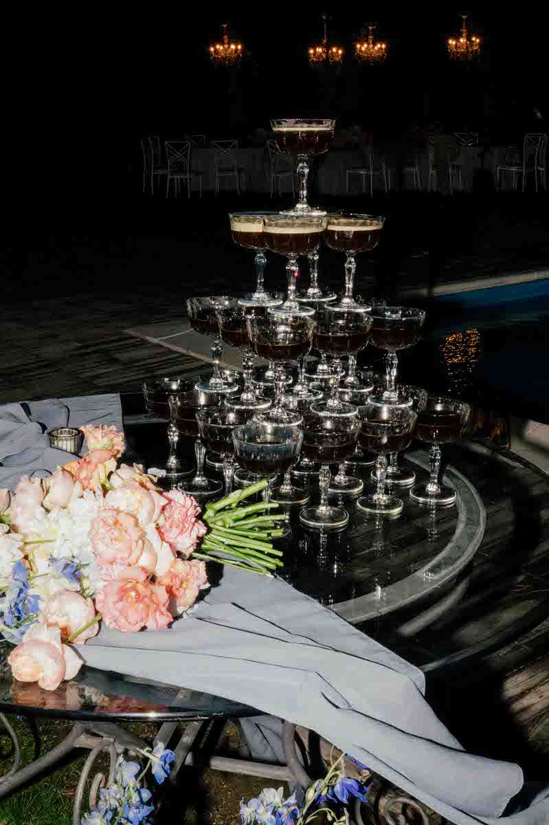 Wedding couple pouring champagne tower with sparkler effects at night celebration.