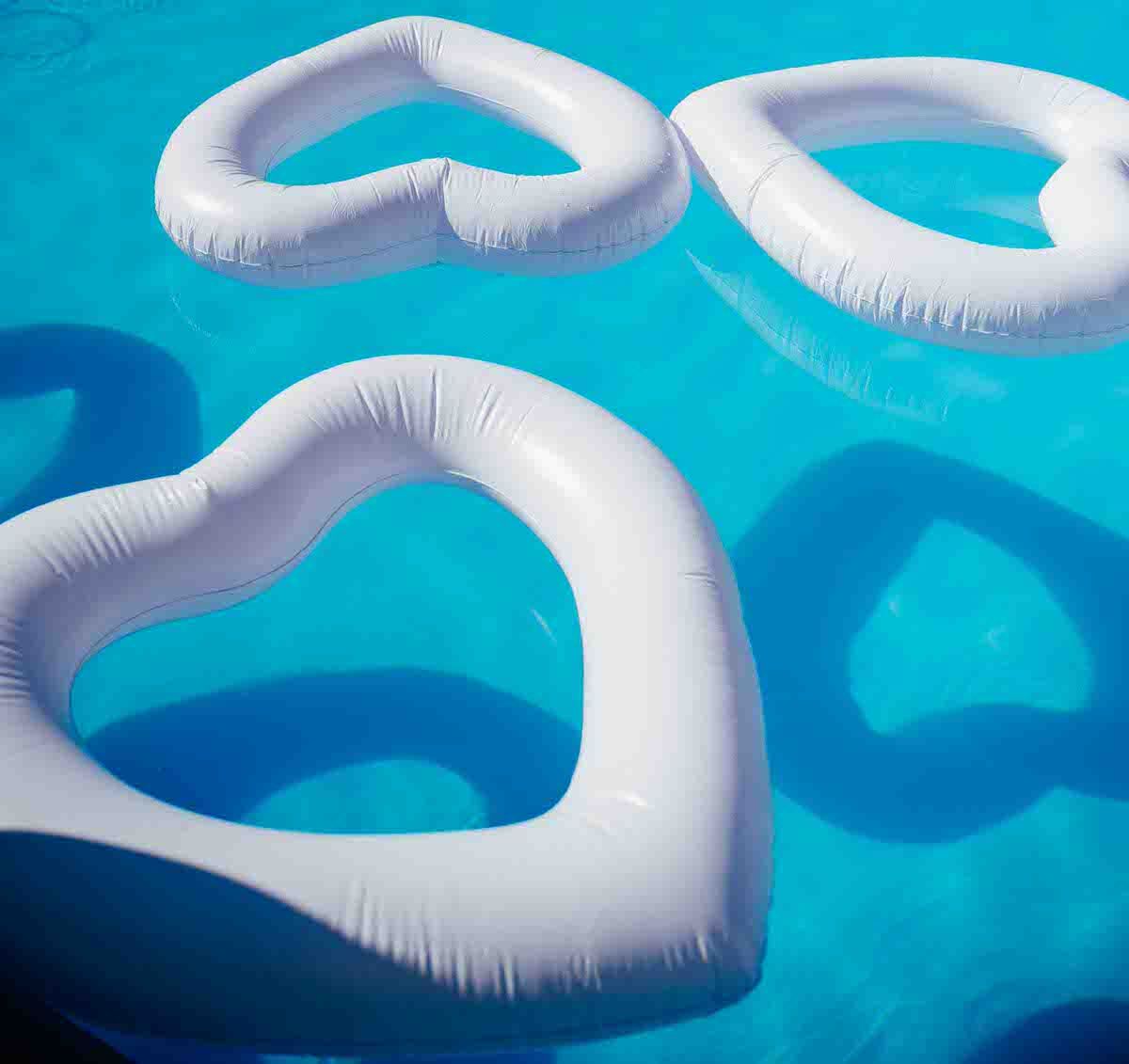White heart-shaped pool floats casting shadows in bright blue swimming pool water.