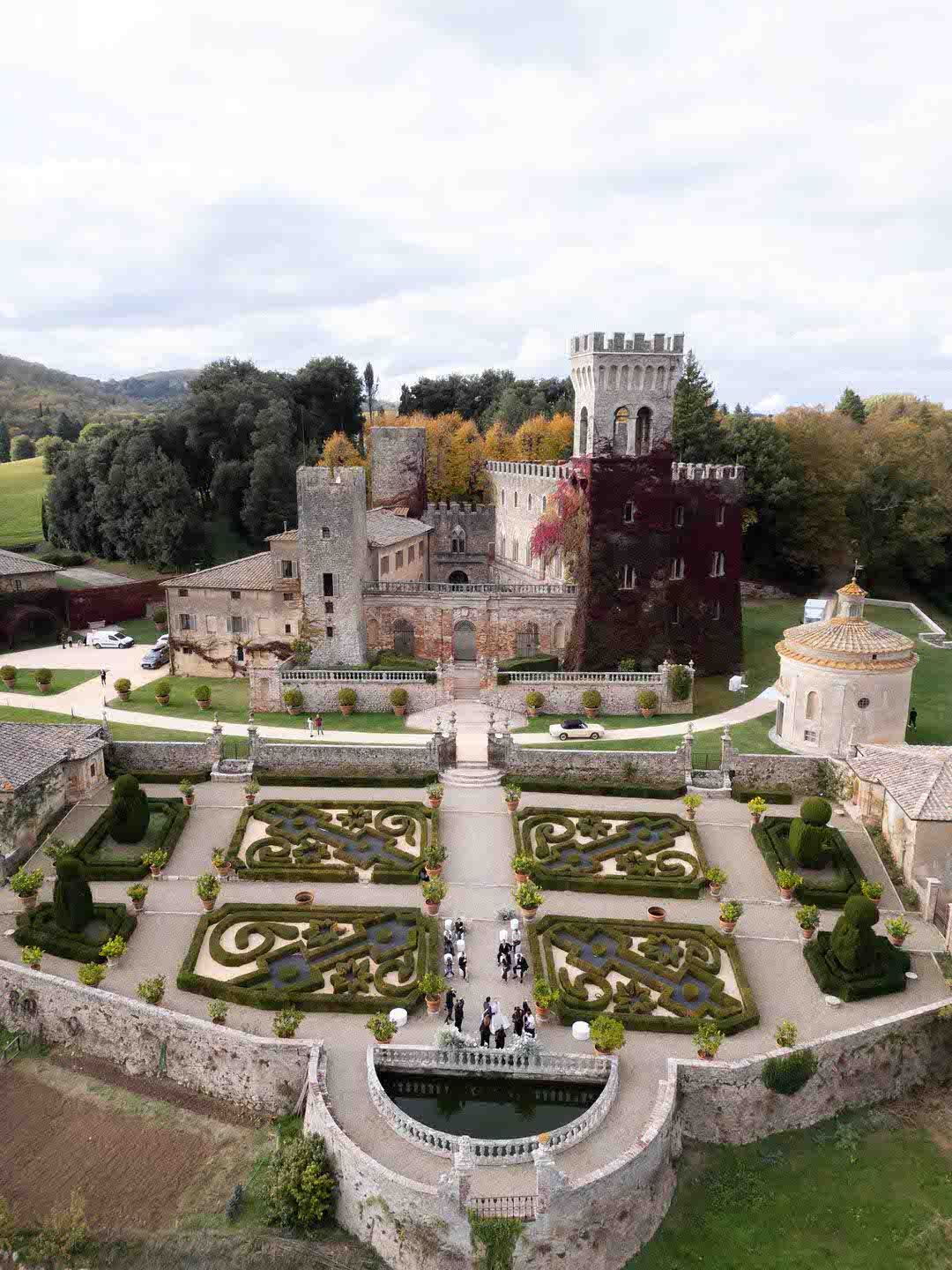 Aerial view of a medieval castle with ornate formal gardens featuring geometric topiary patterns in a lush landscape.