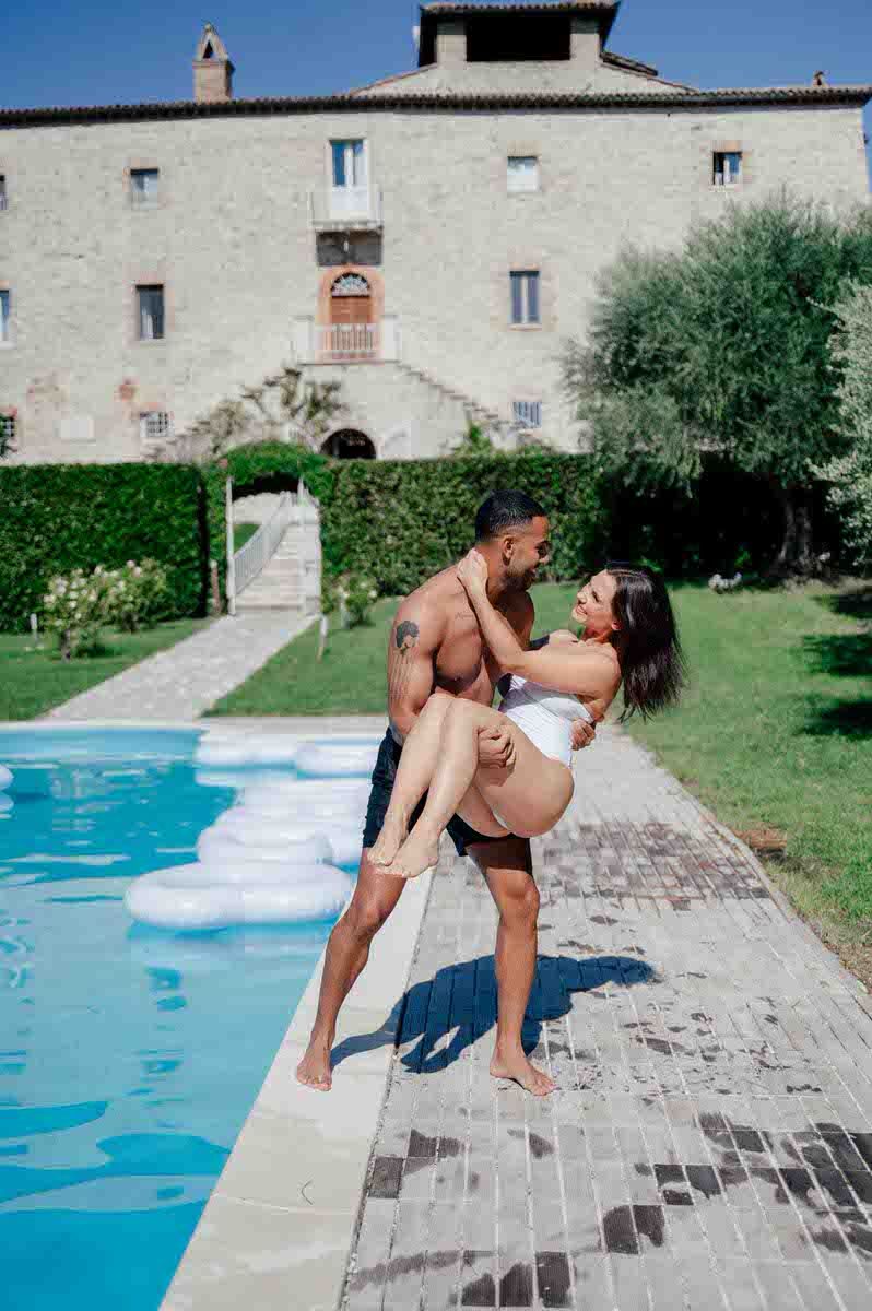 Couple embracing by a luxurious pool with historic Italian villa in the background.