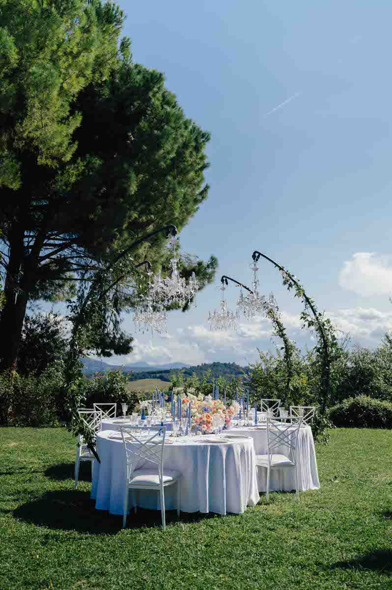 Outdoor wedding reception setup with white tables and chairs under blue sky.
