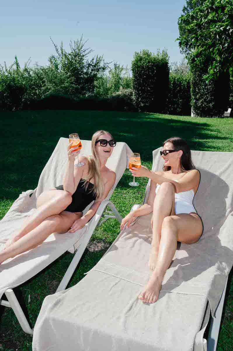 Two friends relaxing on lounge chairs in a garden while enjoying refreshing drinks on a sunny day.