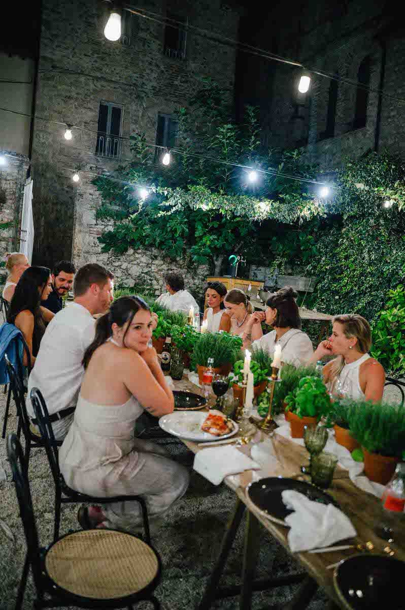 Intimate candlelit dinner party under string lights against rustic stone wall.